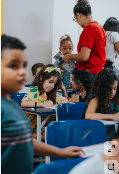 Crianças realizando atividades em sala com acompanhamento de uma educadora.